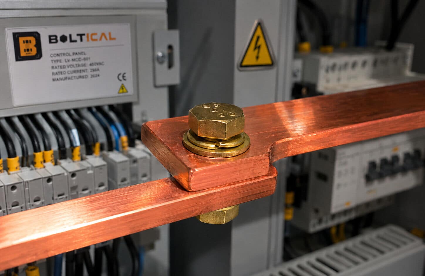 A professional macro photograph capturing the interior of an industrial low-voltage electrical panel. In sharp focus, two bright orange-red copper busbars (شمش مس) are meticulously bolted together using a golden brass hexagonal head bolt, complete with a matching brass flat and spring washer. The background is softly blurred, showing technical electrical wiring, neatly arranged terminal blocks, and a clean corporate graphite-grey control board with subtle safety indicators. A warm, precise studio light gleams off the metallic brass and copper surfaces, creating a high-contrast engineering aesthetic. No sparks, highly realistic, 8k resolution, authentic B2B industrial environment